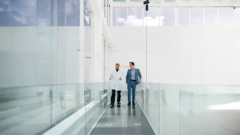 Symboldbild Sparringspartner – Zwei Männer unterhalten sich beim Gehen durch ein modernes Gebäude