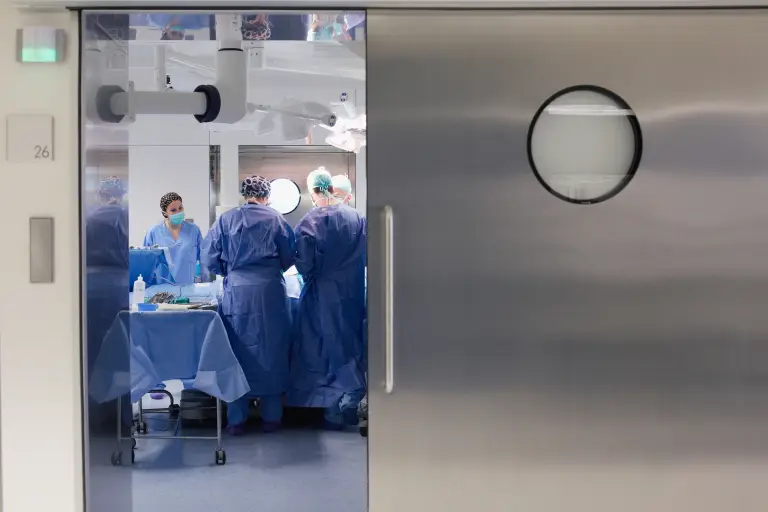 Blick durch eine geöffnete Schiebetür in einen Operationssaal, in dem ein OP-Team arbeitet