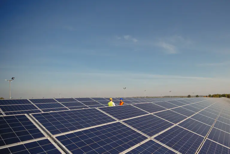 Zwei Techniker mit Schutzhelm zwischen den Modulen einer großen Photovoltaikanlage